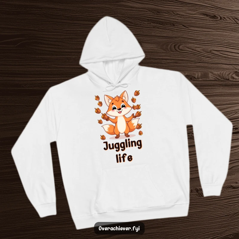 Funny hoodie with a playful fox character grinning while juggling an impossible number of shiny acorns, perfect for cozy fun.